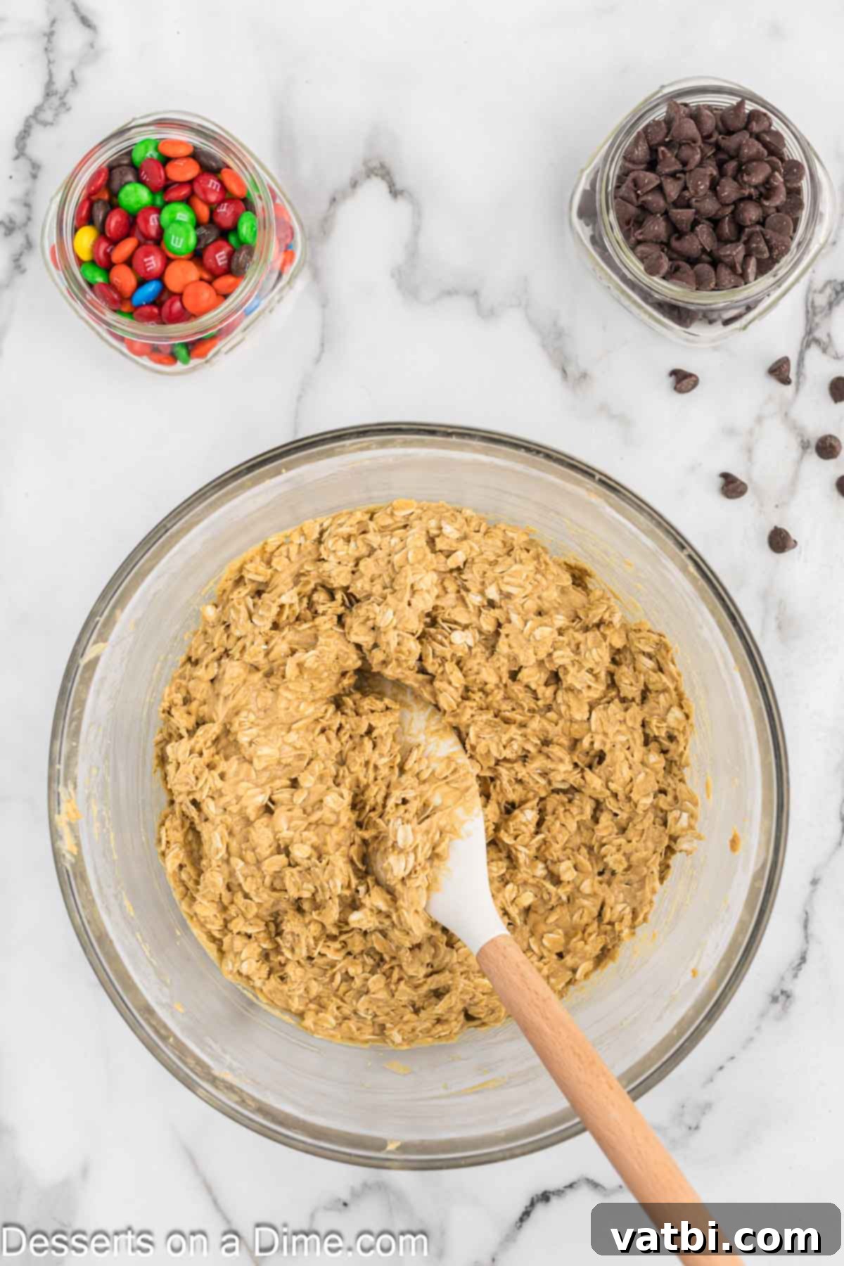 Ultimate Gluten-Free Monster Cookies 5 Old-fashioned oats being added to the mixed cookie dough in a bowl, preparing for final mixing.