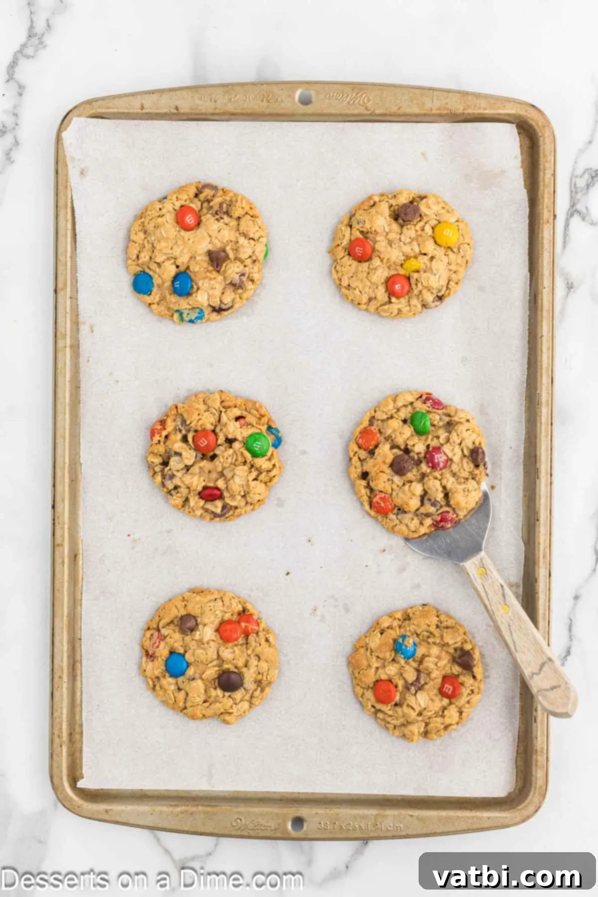 Ultimate Gluten-Free Monster Cookies 8 Freshly baked gluten-free monster cookies cooling on a baking sheet, showing golden-brown edges and soft centers.