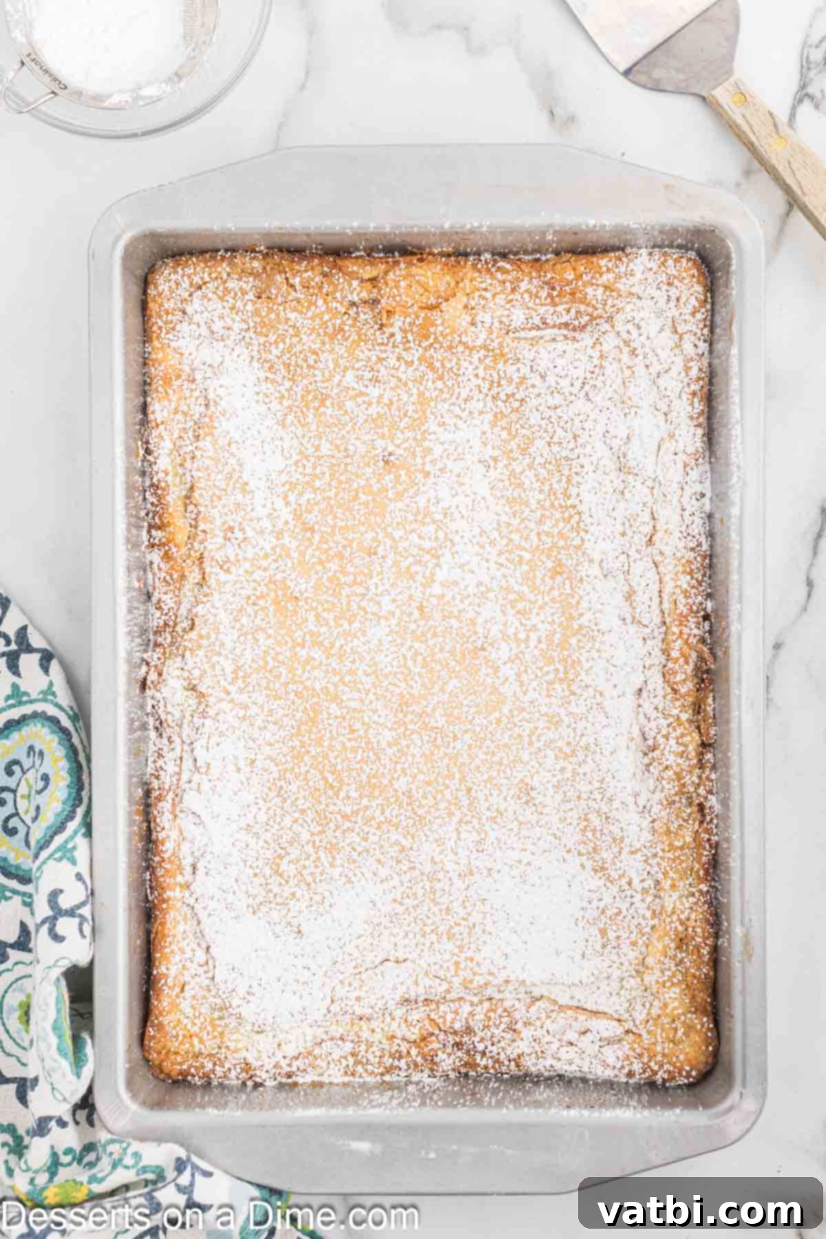 Paula Deen's Signature Ooey Gooey Butter Cake 10 Powdered sugar being sprinkled on top of the cooled Ooey Gooey Butter Cake.