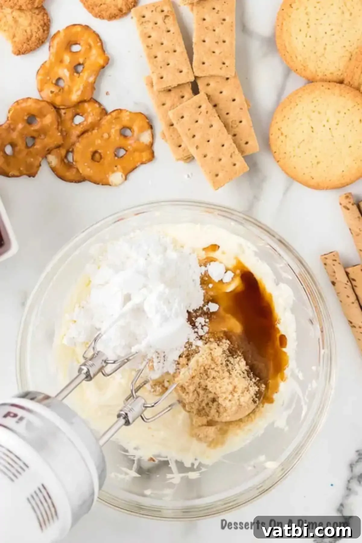 A mixing bowl containing the cream cheese and butter mixture, with powdered sugar, brown sugar, and vanilla extract being added on top.