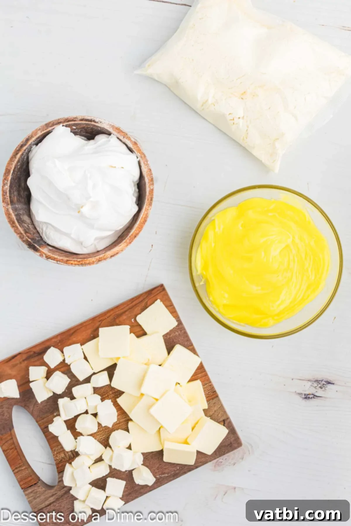 Effortless Lemon Delight 4 Ingredients for Lemon Dump Cake including a box of yellow cake mix, a block of cream cheese, sticks of butter, and a tub of cool whip, arranged on a rustic wooden surface.