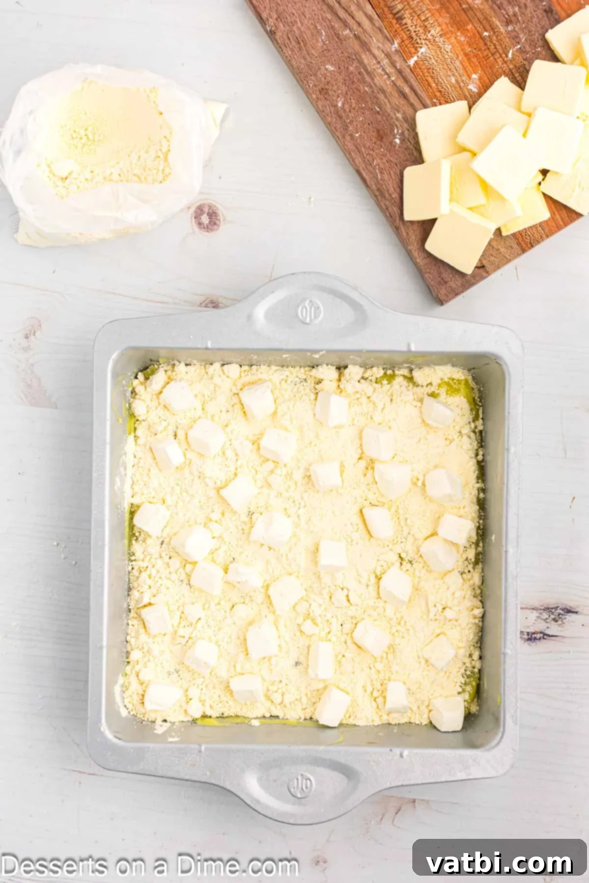 Effortless Lemon Delight 7 Small, diced pieces of cream cheese are scattered over the half-sprinkled cake mix layer in the baking pan.