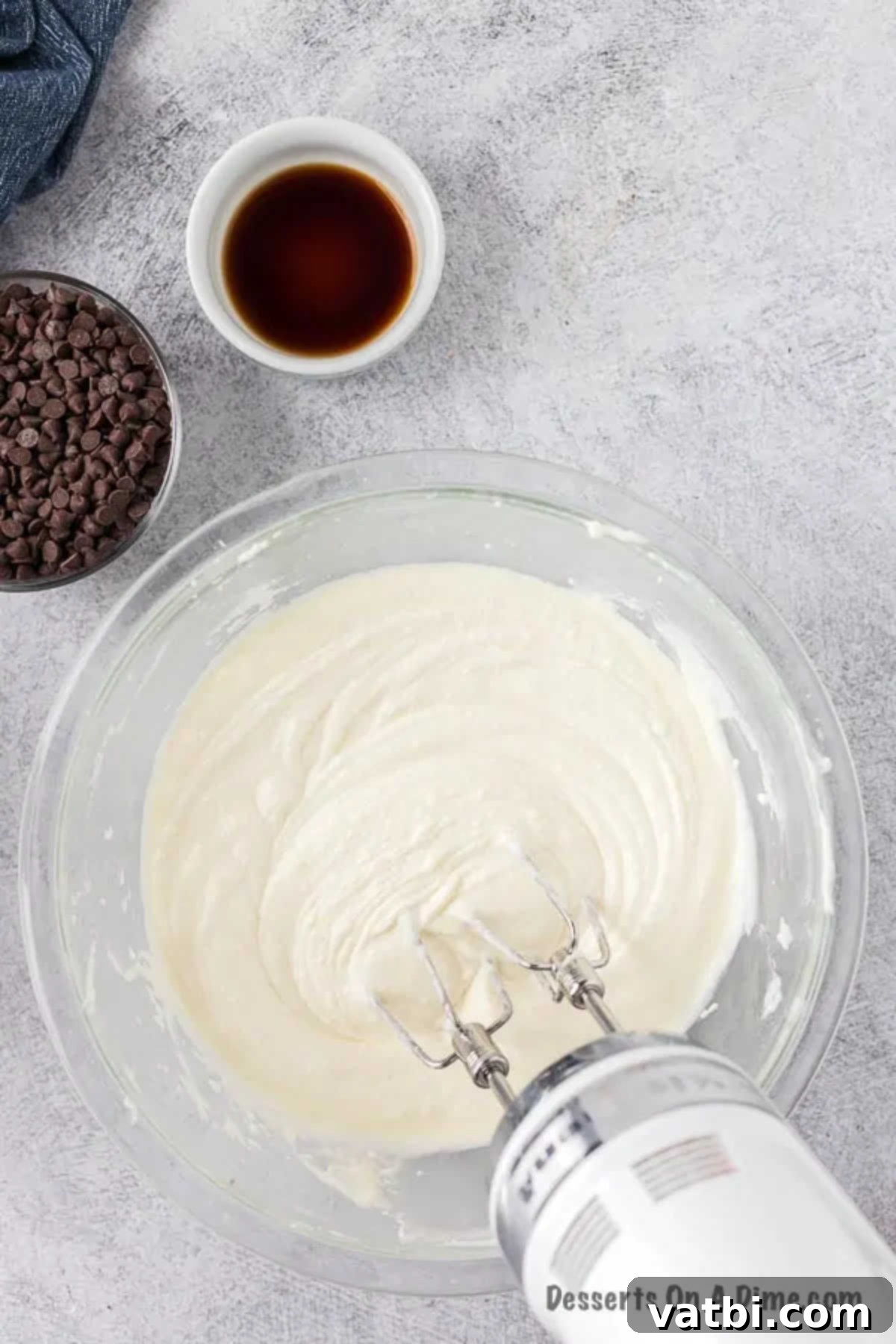 Decadent Cannoli Dip 4 A smooth, creamy mixture of softened cream cheese, ricotta, and powdered sugar being whipped in a large mixing bowl with an electric mixer.