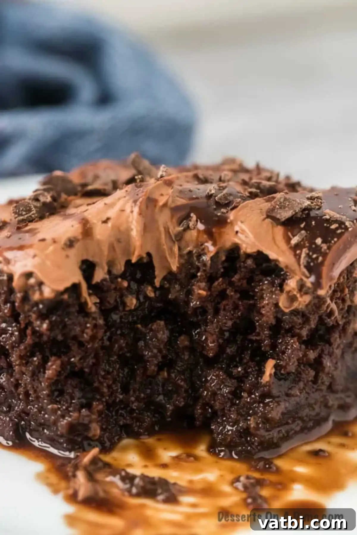 A perfectly sliced piece of chocolate poke cake, showing its moist layers and rich topping, served on a white plate, ready to be enjoyed.
