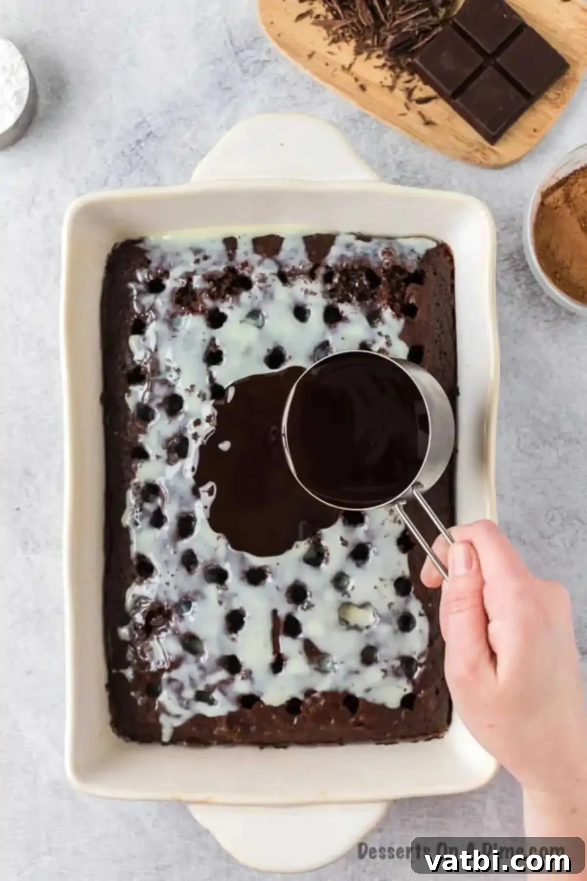 Sweetened condensed milk and rich chocolate sauce being poured generously over a freshly poked chocolate cake, ensuring maximum absorption and flavor.