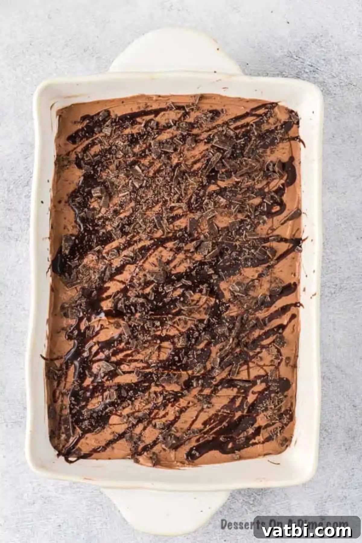 The finished chocolate poke cake, generously topped with creamy chocolate frosting and drizzled with extra chocolate sauce, adorned with chopped chocolate pieces.