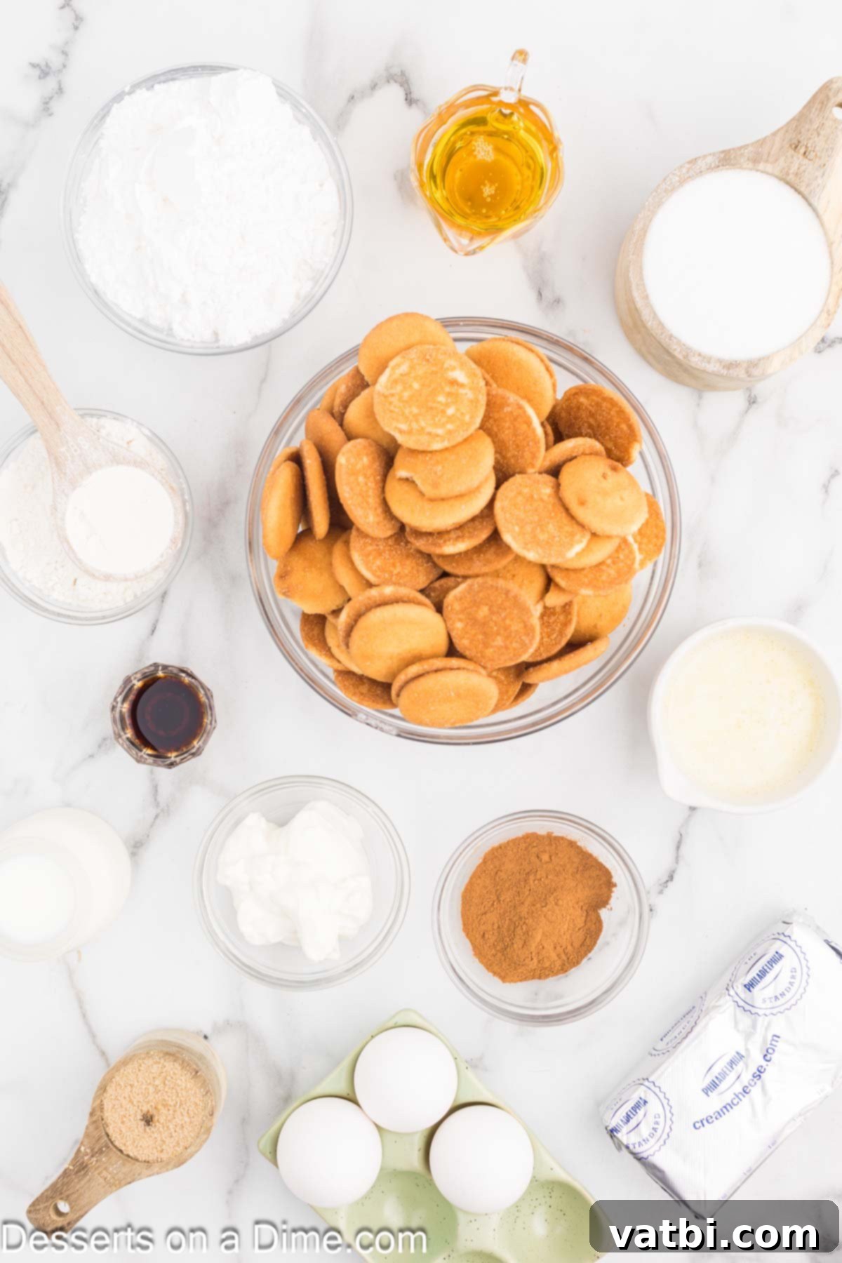 Honey Cinnamon Swirl Cheesecake 3 A collection of ingredients laid out for Honey Bun Cheesecake including vanilla wafers, butter, ground cinnamon, cream cheese, eggs, sour cream, honey, vanilla extract, flour, brown sugar, powdered sugar, and milk.