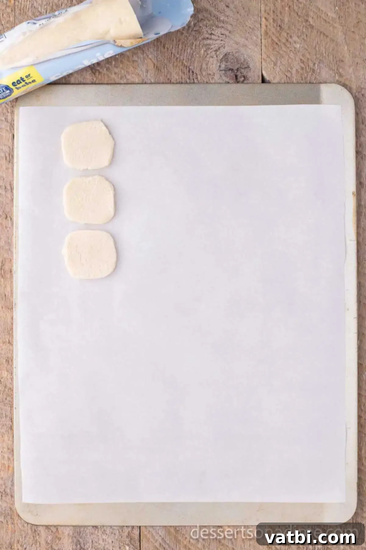 Effortless Snowman Cookie Fun 3 Individual portions of store-bought cookie dough arranged on a parchment-lined baking sheet.