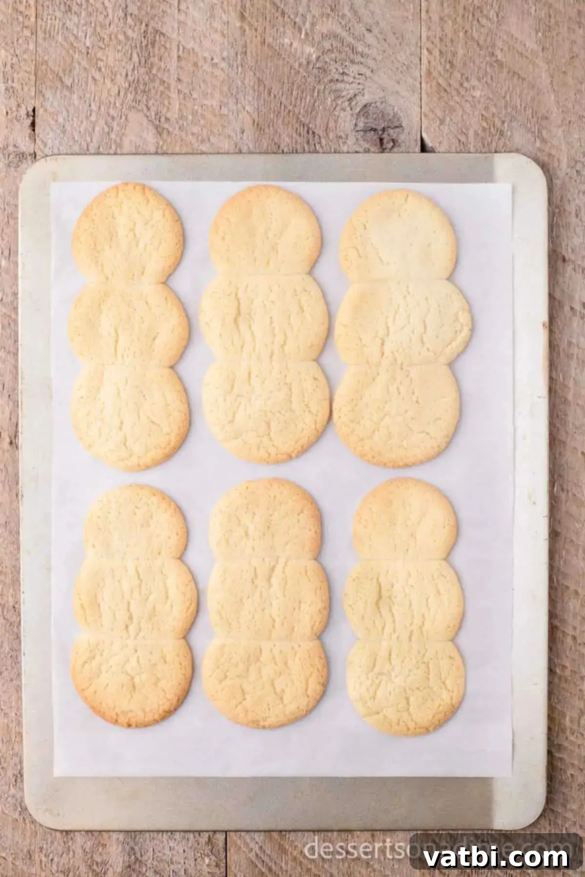 Effortless Snowman Cookie Fun 5 Golden-brown snowman-shaped sugar cookies fresh out of the oven, cooling on a baking sheet.