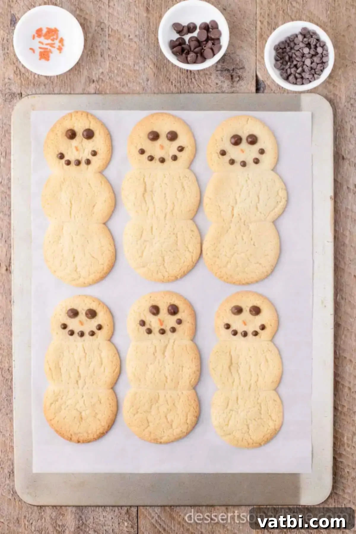 Effortless Snowman Cookie Fun 6 Warm snowman cookies with mini chocolate chips placed for eyes and regular chocolate chips for the mouth.