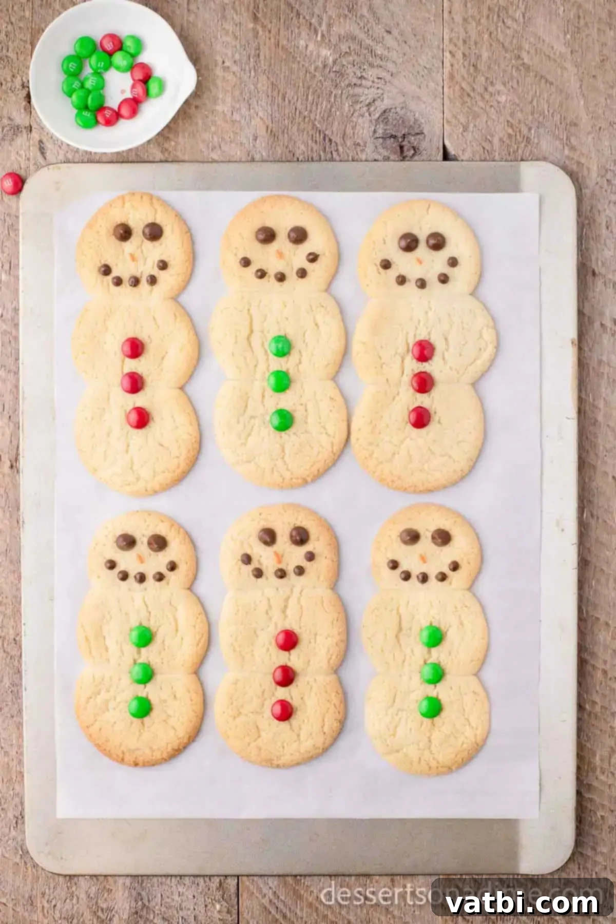 Effortless Snowman Cookie Fun 7 Snowman cookies decorated with chocolate chip eyes and mouth, and colorful M&M candies for buttons.