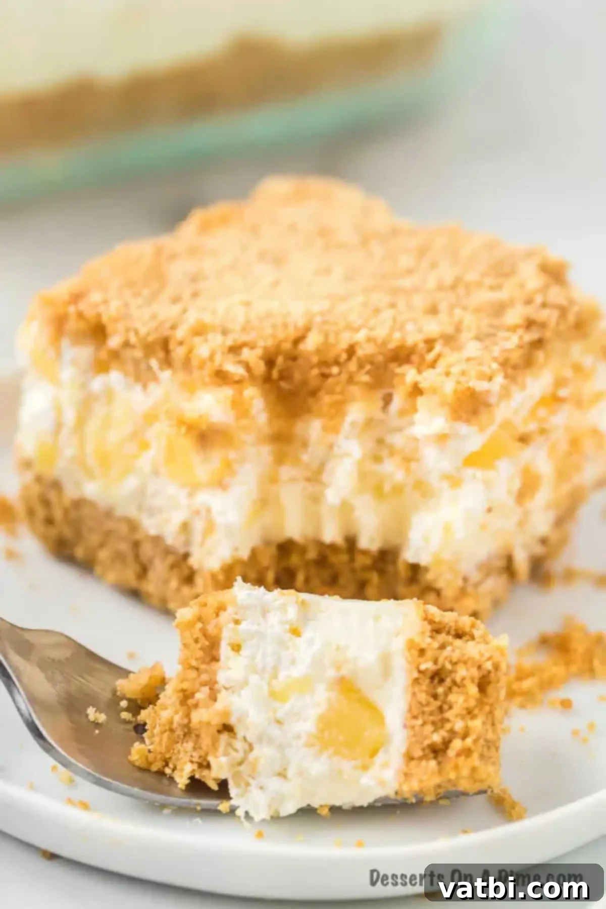 Golden Pineapple Bliss 10 A perfect slice of Pineapple Dream Dessert, showcasing its distinct layers of golden crust, creamy pineapple filling, and fluffy whipped topping, served on a white plate.