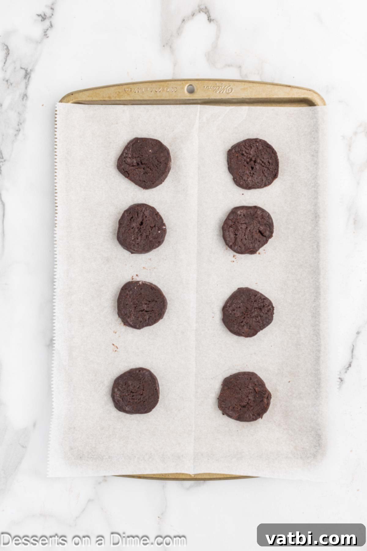 Layered Chocolate Delights 10 Uniformly sliced chocolate wafer cookie dough rounds arranged on a parchment-lined baking sheet, ready for the oven.