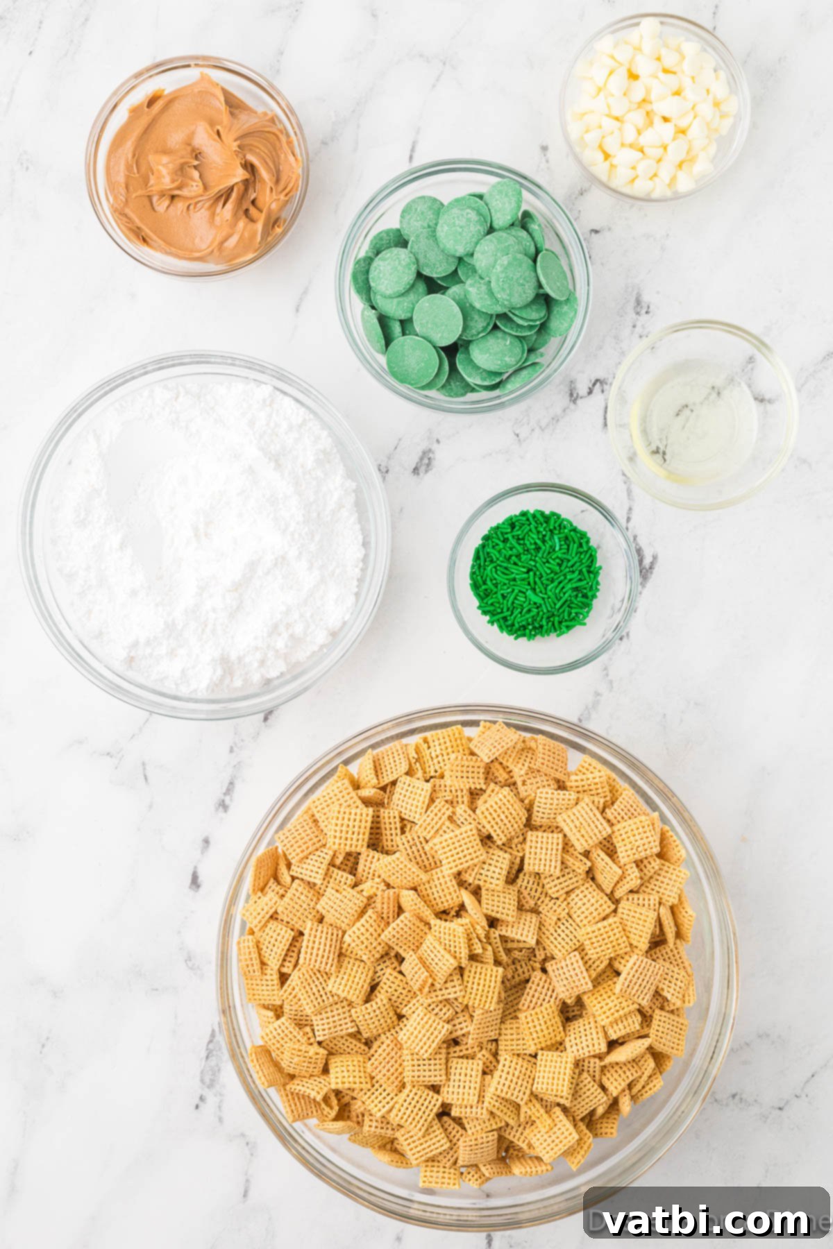 A selection of ingredients for St. Patrick's Day Puppy Chow laid out: Chex cereal, creamy peanut butter, green candy melts, powdered sugar, festive green sprinkles, and colorful green M&Ms.