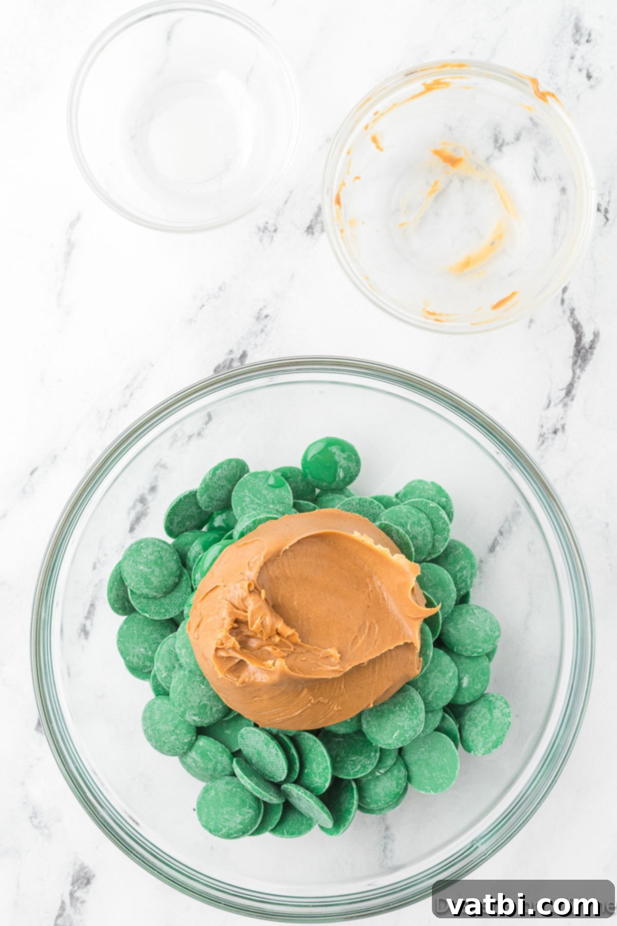 A microwave-safe bowl with green candy melts, peanut butter, and vegetable oil combined and ready for melting.