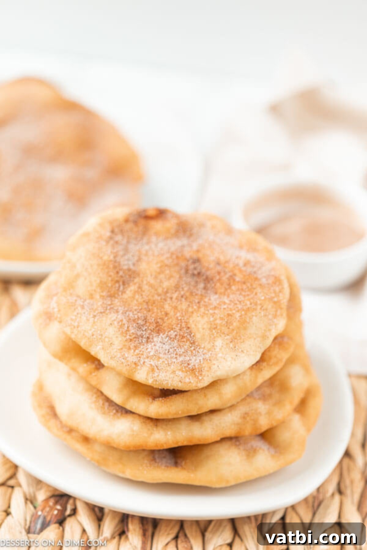 Homemade Elephant Ear Perfection 2 Four golden-brown elephant ears stacked on a white serving plate, generously topped with a glistening cinnamon sugar mixture, ready to be enjoyed.