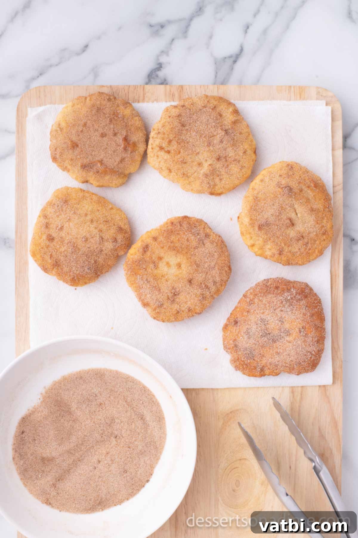 Homemade Elephant Ear Perfection 13 A generous sprinkling of cinnamon sugar mixture falling onto freshly fried elephant ears that are still warm and resting on paper towels, ensuring the topping adheres perfectly.