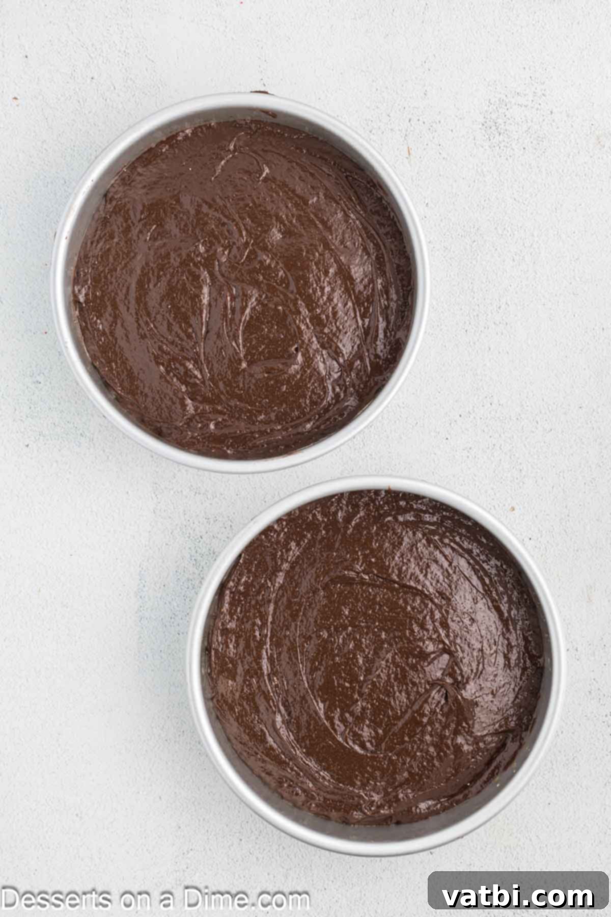 Evenly poured chocolate cake batter in two round baking pans, ready for the oven.