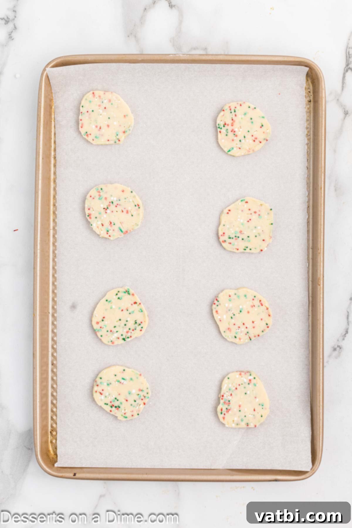 Yuletide Shortbread Delights 8 Uniformly sliced shortbread cookie dough rounds carefully placed on a parchment-lined baking sheet.