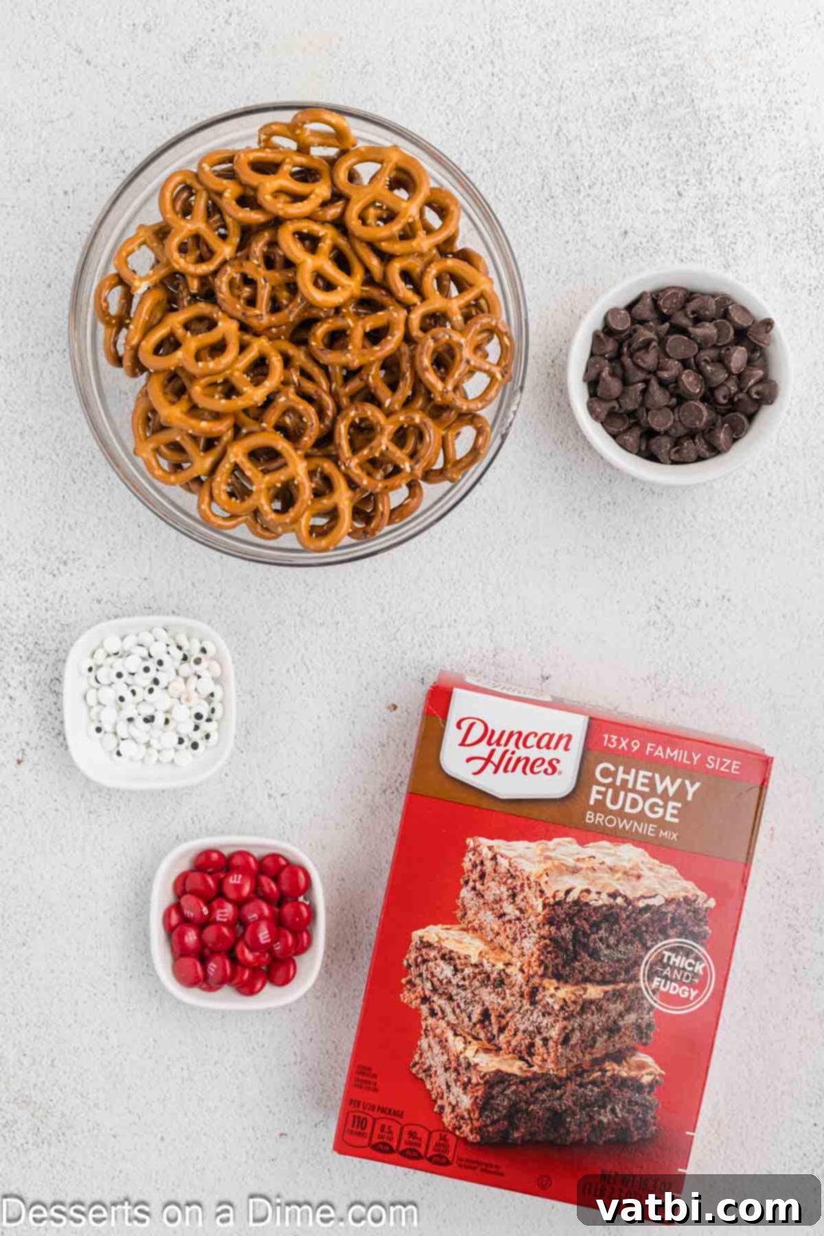 Reindeer Brownies 3 Ingredients for Reindeer Brownie Mix - box brownie mix and ingredients to prepare brownies, chocolate chips, mini pretzels, candy eyes, red M&Ms, all laid out on a white surface.