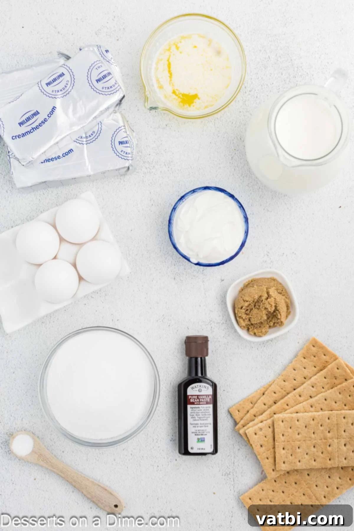 Golden Crown Cheesecake 3 A flat lay of fresh ingredients for Cheesecake Brulee, including graham cracker sheets, butter, brown sugar, cream cheese, vanilla bean pods, large eggs, heavy cream, sour cream, and granulated sugar.