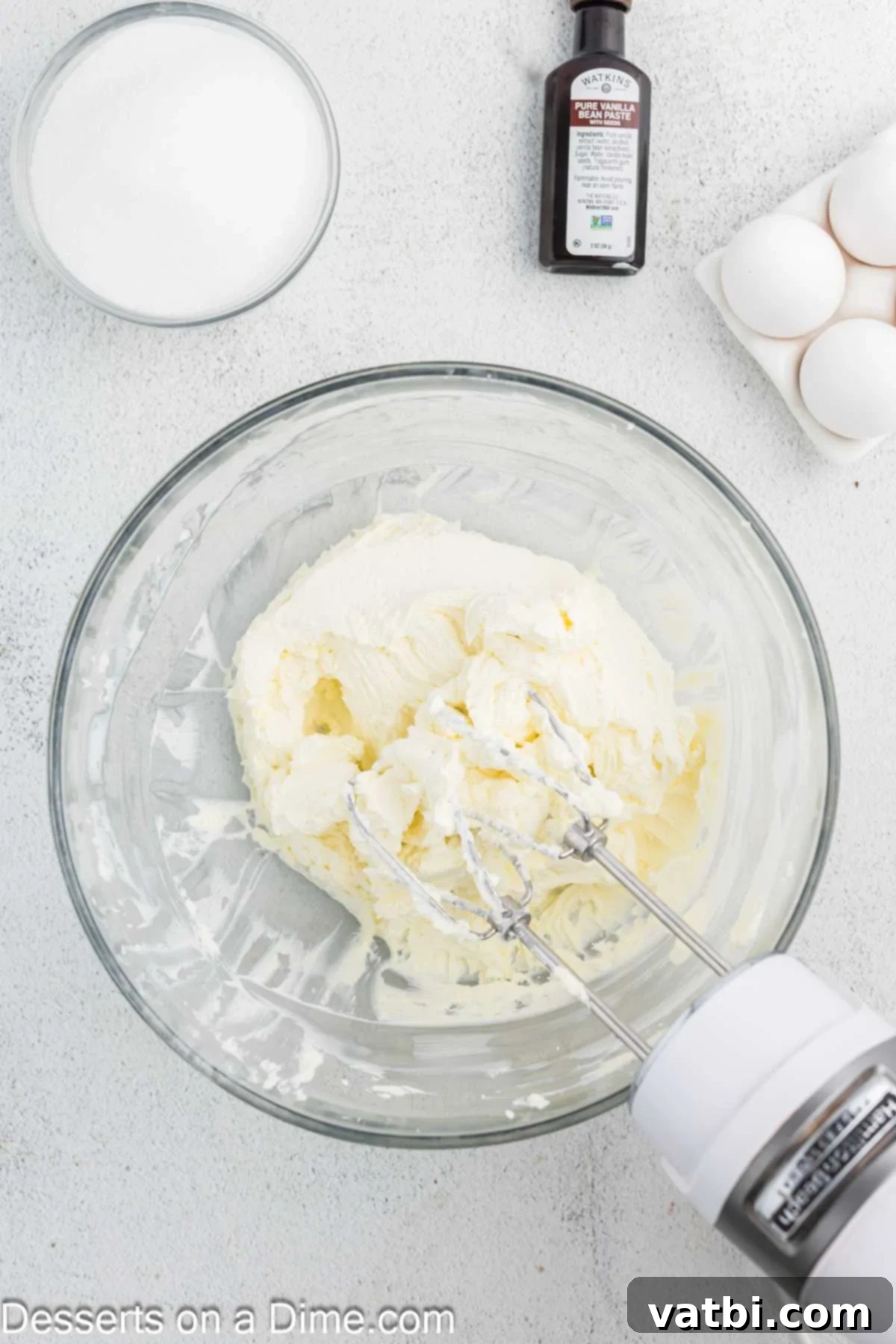 Golden Crown Cheesecake 6 Softened cream cheese being beaten until fluffy and smooth in a large mixing bowl with an electric mixer.