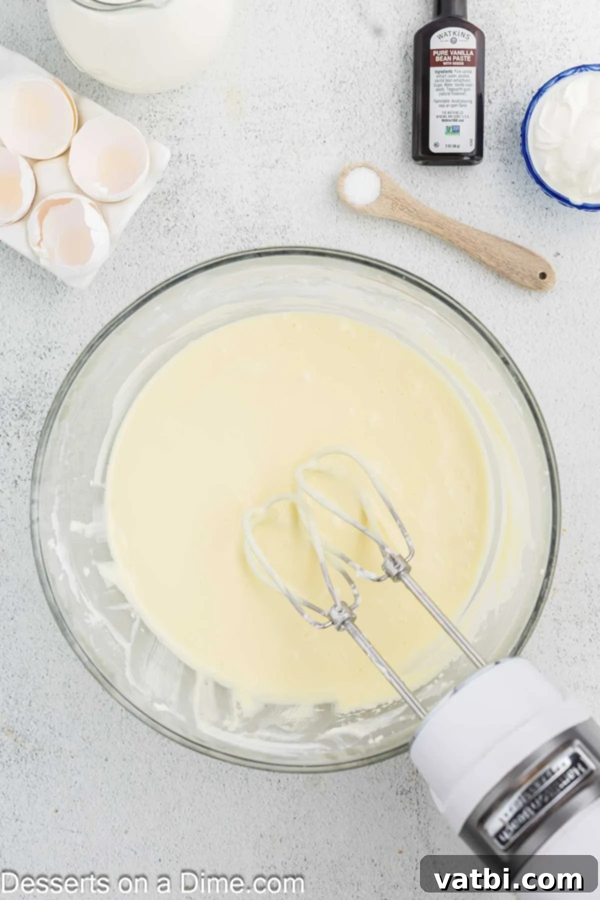 Golden Crown Cheesecake 7 Eggs being slowly mixed into the cream cheese and sugar batter, one at a time, to ensure proper emulsification.
