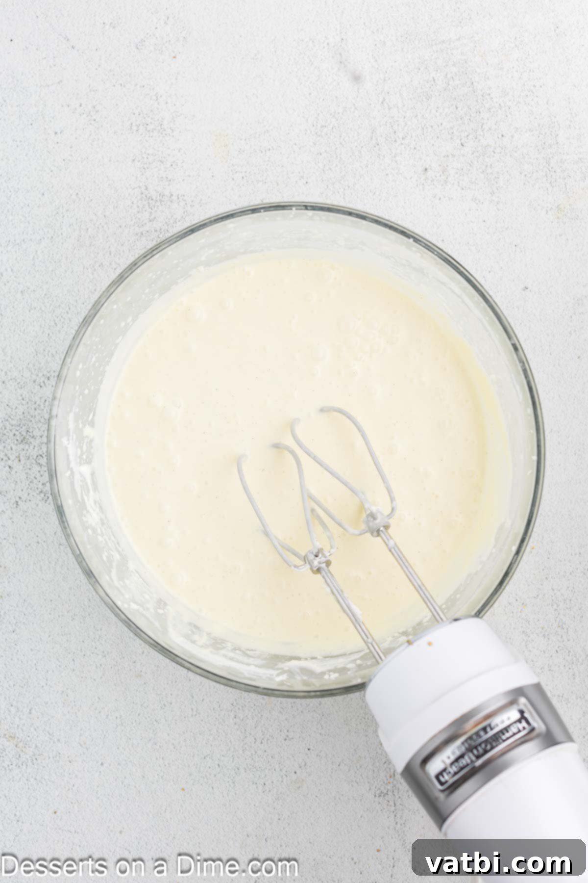 Golden Crown Cheesecake 8 Sour cream and heavy cream being gently folded into the cheesecake batter with an electric mixer on low speed.