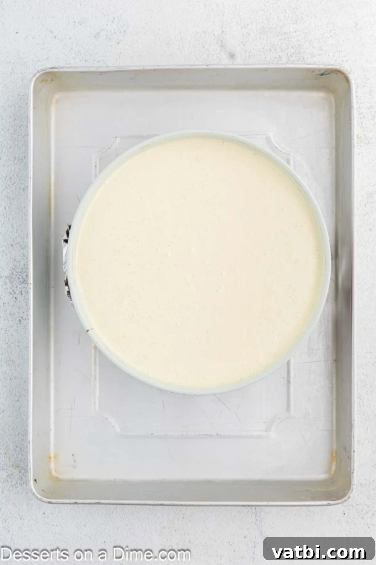 Golden Crown Cheesecake 9 Cheesecake batter poured over the crust in a springform pan, wrapped in foil and placed in a water bath, ready for baking.