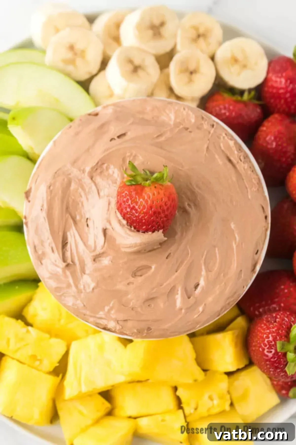 Chocolatey Fruit Indulgence 8 A beautifully presented chocolate fruit dip in a white bowl, generously surrounded by an array of colorful fresh fruits and some crunchy graham crackers.