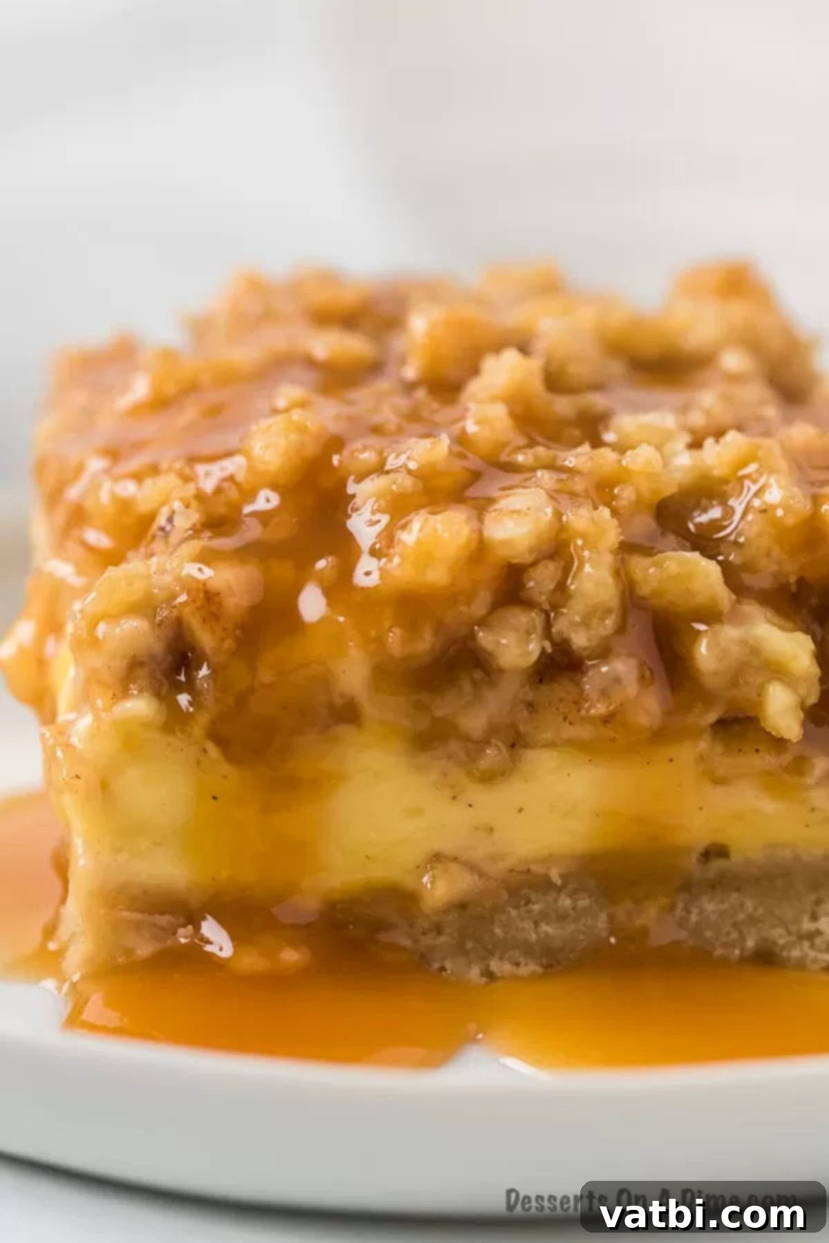 Harvest Caramel Apple Cheesecake Bars 2 Close up image of a golden-brown Caramel Apple Cheesecake bar with a generous caramel drizzle, resting on a white plate, showcasing its delicious layers and crumbly topping.