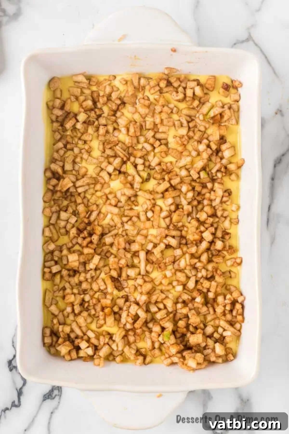 Harvest Caramel Apple Cheesecake Bars 11 The spiced apple mixture spread evenly over the cheesecake batter in the baking dish, forming a distinct middle layer of the dessert bars.
