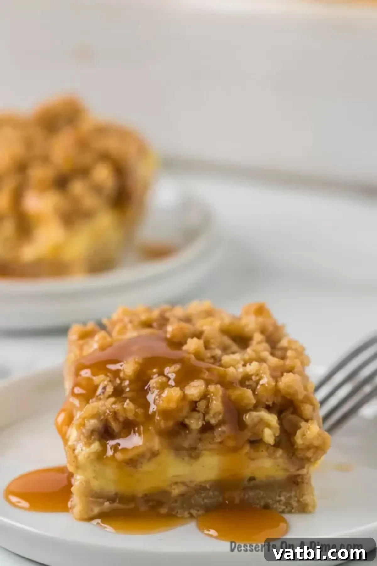 Harvest Caramel Apple Cheesecake Bars 16 Close up image of a golden-brown Caramel Apple Cheesecake bar with a generous caramel drizzle, resting on a white plate, showcasing its delicious layers and crumbly topping.