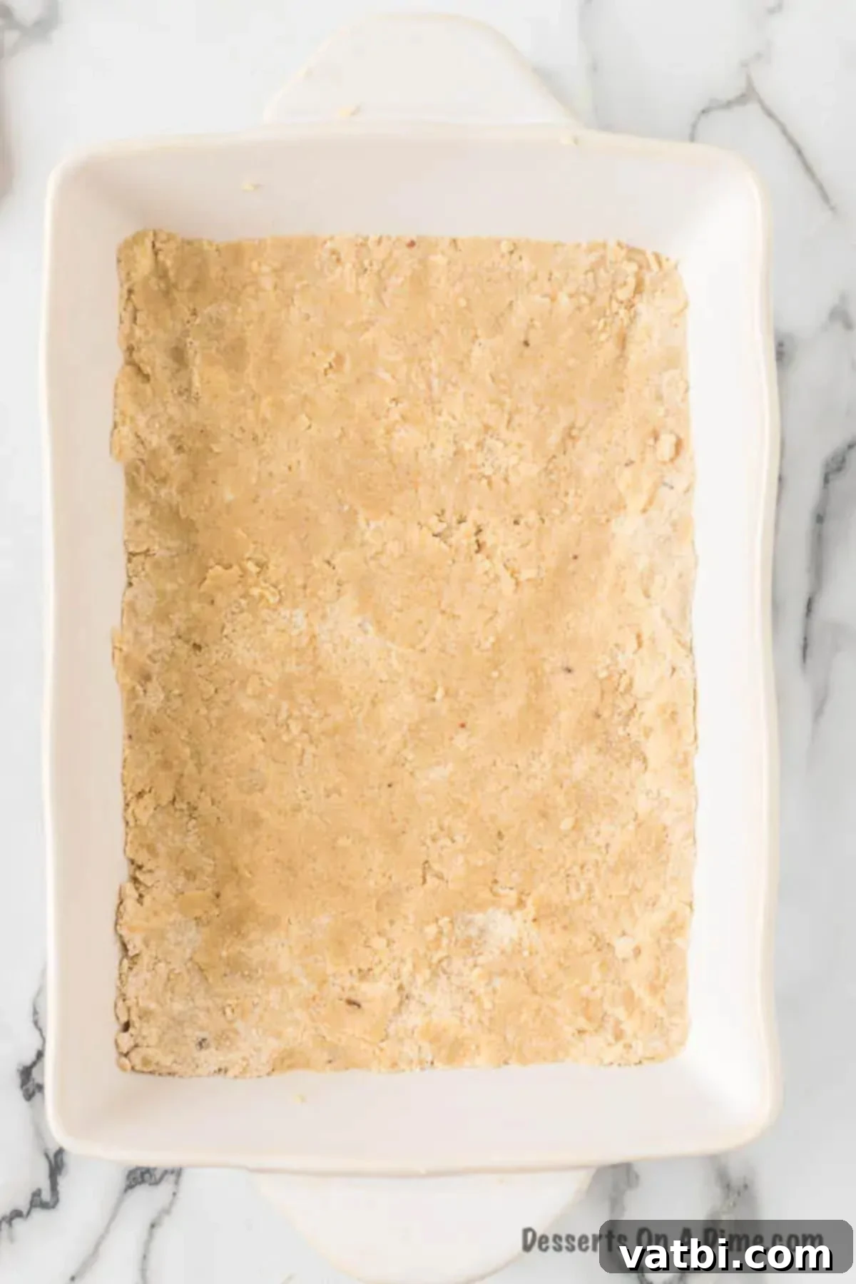 Harvest Caramel Apple Cheesecake Bars 6 The crumbly shortbread crust mixture evenly pressed into the bottom of a 9x13 inch baking pan, ready for its initial bake.