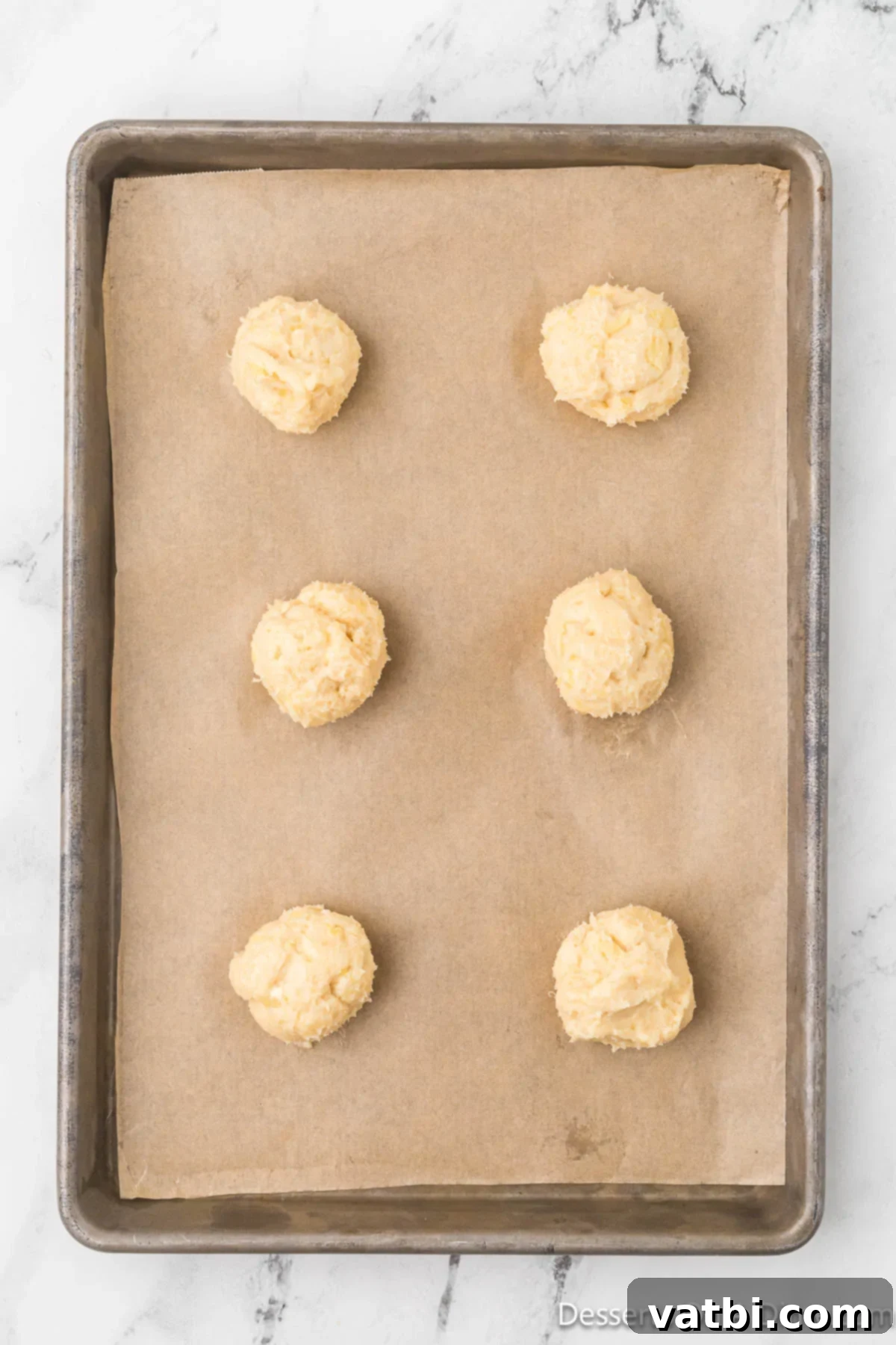 Cookie dough scooped into uniform balls and placed on a parchment-lined baking sheet.
