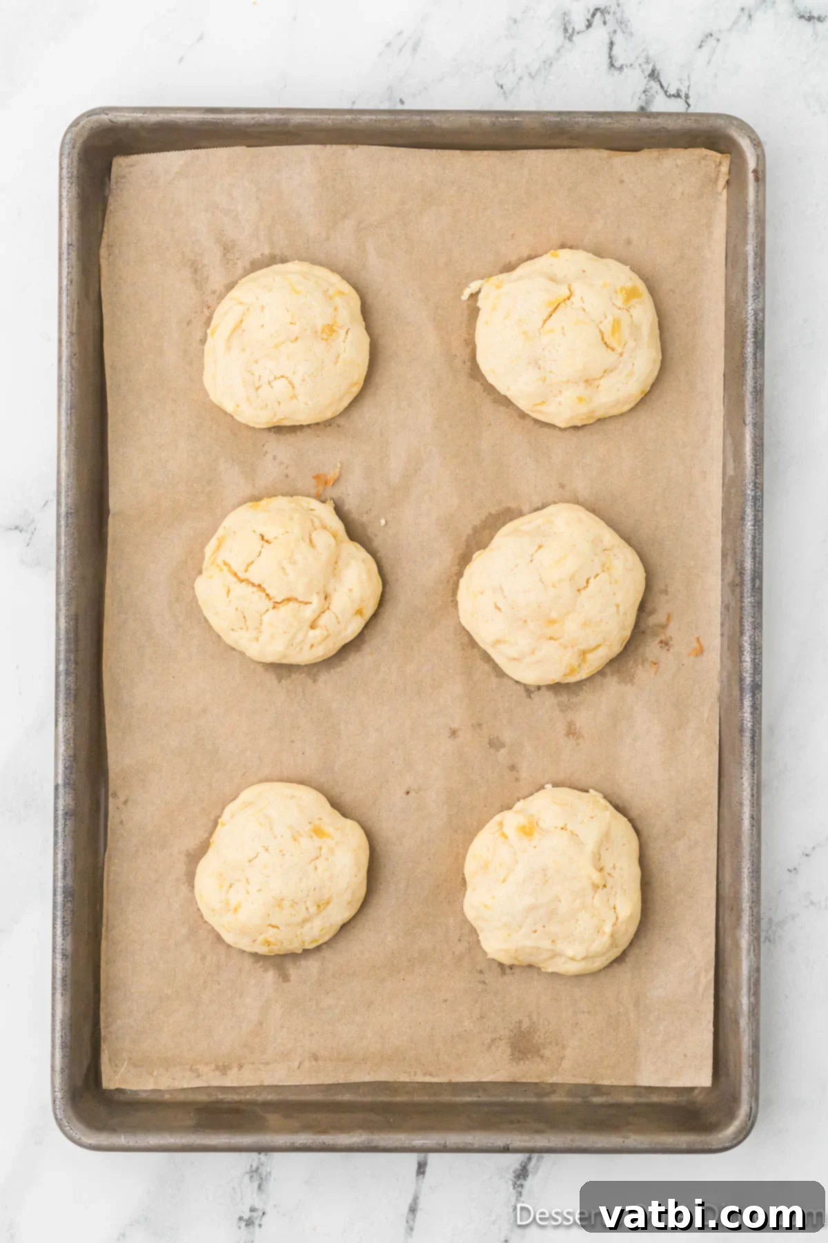 Freshly baked pineapple cookies cooling on a baking sheet.