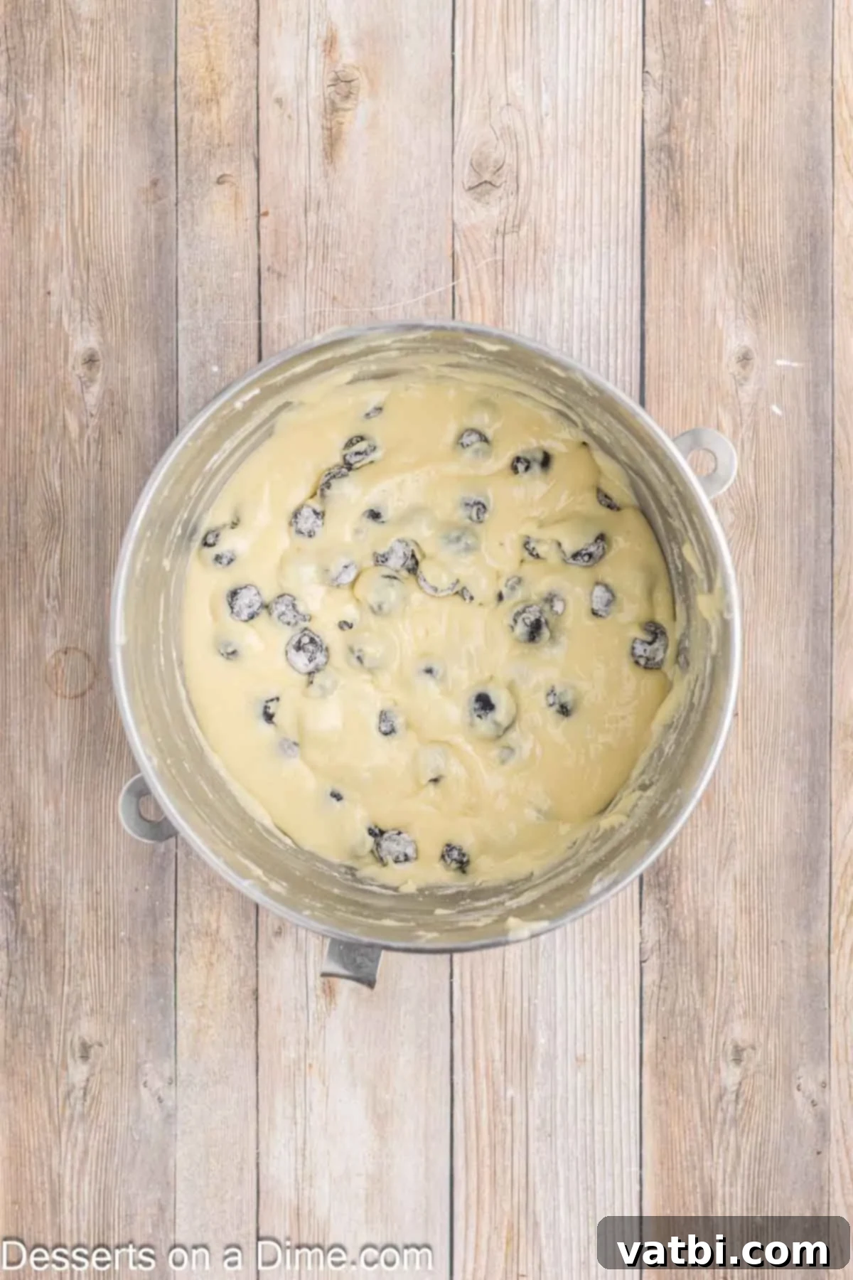 Blueberry Crown Cake 6 Plump blueberries, lightly coated in flour, being gently folded into the smooth blueberry cake batter using a rubber spatula in a large mixing bowl, ensuring even distribution.