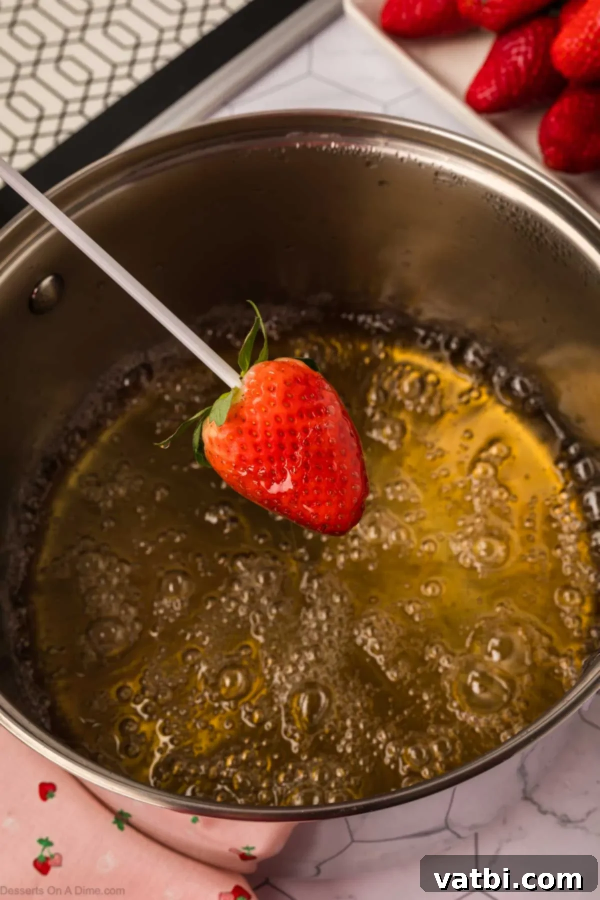 Glossy Strawberry Treats 6 A strawberry being dipped into the hot candied sugar mixture using a skewer.
