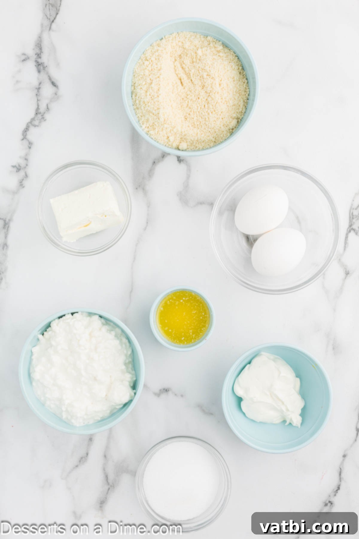 Rustic Farmhouse Cheesecake 3 Ingredients for cottage cheese cheesecake neatly laid out: almond flour, butter, monk fruit sweetener, cottage cheese, Greek yogurt, cream cheese, and eggs.