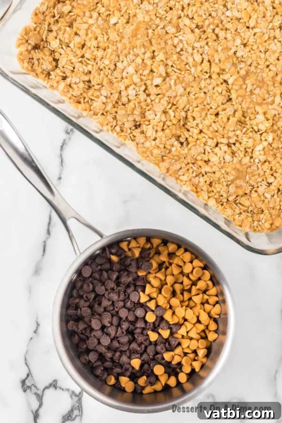 A 9x13 inch pan filled with the cereal-peanut butter mixture, next to a small saucepan with melting chocolate and butterscotch chips.