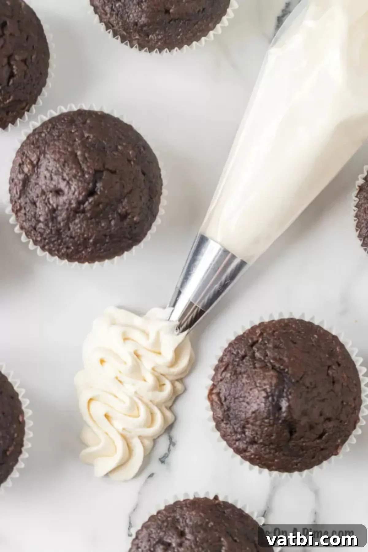 Piping bag filled with marshmallow frosting, with perfectly frosted chocolate cupcakes in the background.