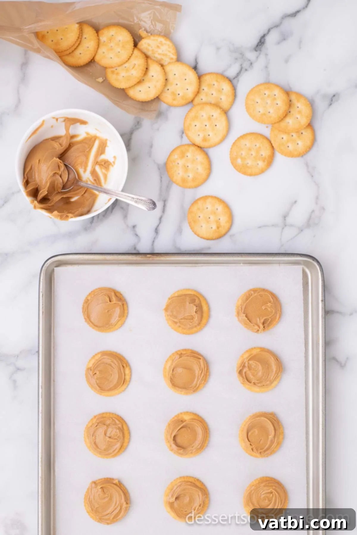 Sweet and Salty Chocolate Ritz Bites 3 Creamy peanut butter being spread evenly onto one half of Ritz crackers, laid out on a baking sheet, ready for sandwiching.