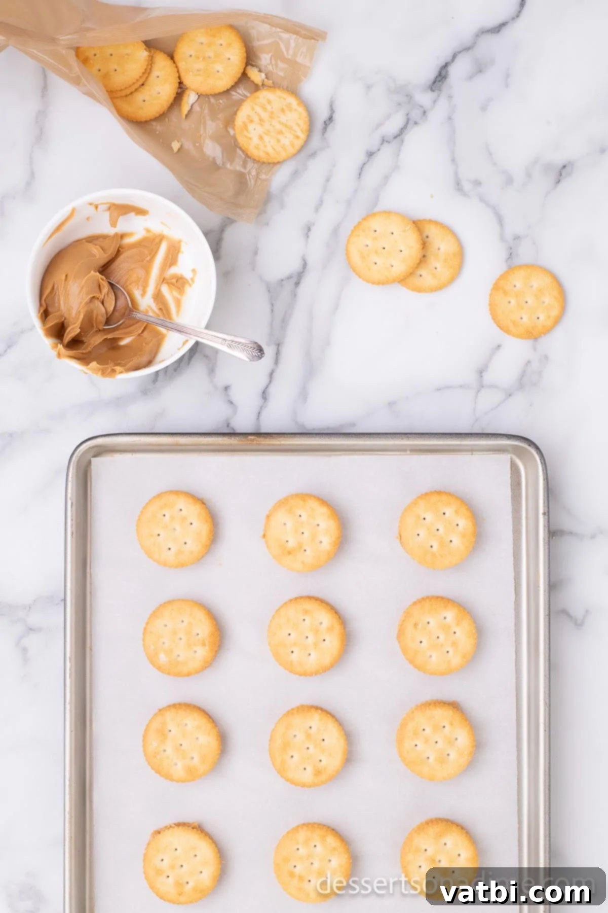 Sweet and Salty Chocolate Ritz Bites 4 Two Ritz crackers, expertly filled with creamy peanut butter, forming a neat sandwich on a baking sheet lined with parchment paper, awaiting their chocolate coating.