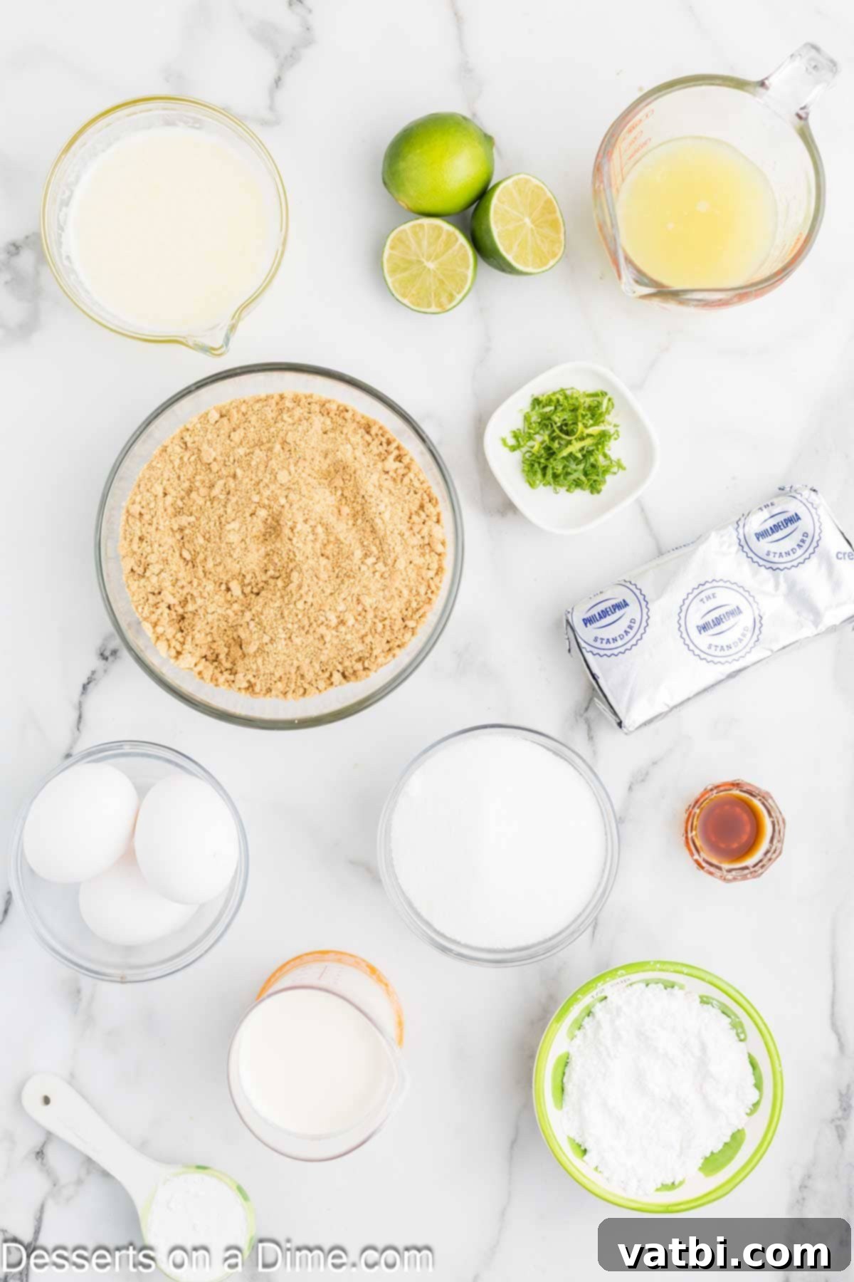 Key Lime Cheesecake 3 Ingredients for key lime cheesecake- graham cracker crumbs, sugar, butter, cream cheese, sugar, cornstarch, lime, heavy cream, powdered sugar, vanilla, spread out on a counter.