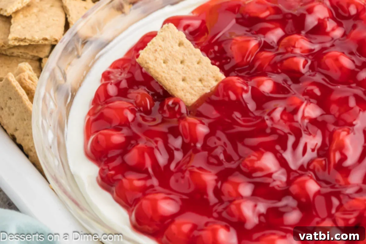 Creamy Cherry Dream Dip 2 Cherry Cheesecake Dip in a decorative dish, surrounded by graham crackers and fresh berries, ready for serving at a party.