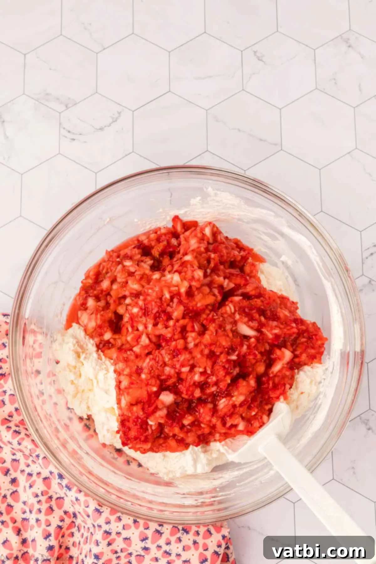 Finely diced fresh strawberries being mixed into the creamy cheesecake fluff base.