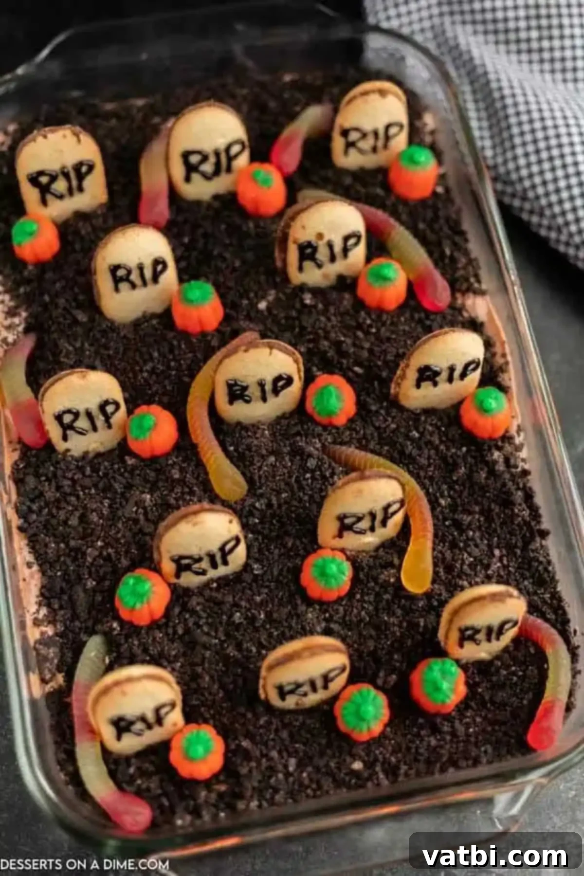 Spooky Halloween Dirt Cake 2 A finished Halloween Dirt Cake in a baking dish, adorned with gummy worms, candy pumpkins, and Milano cookie tombstones, ready to serve at a spooky party.