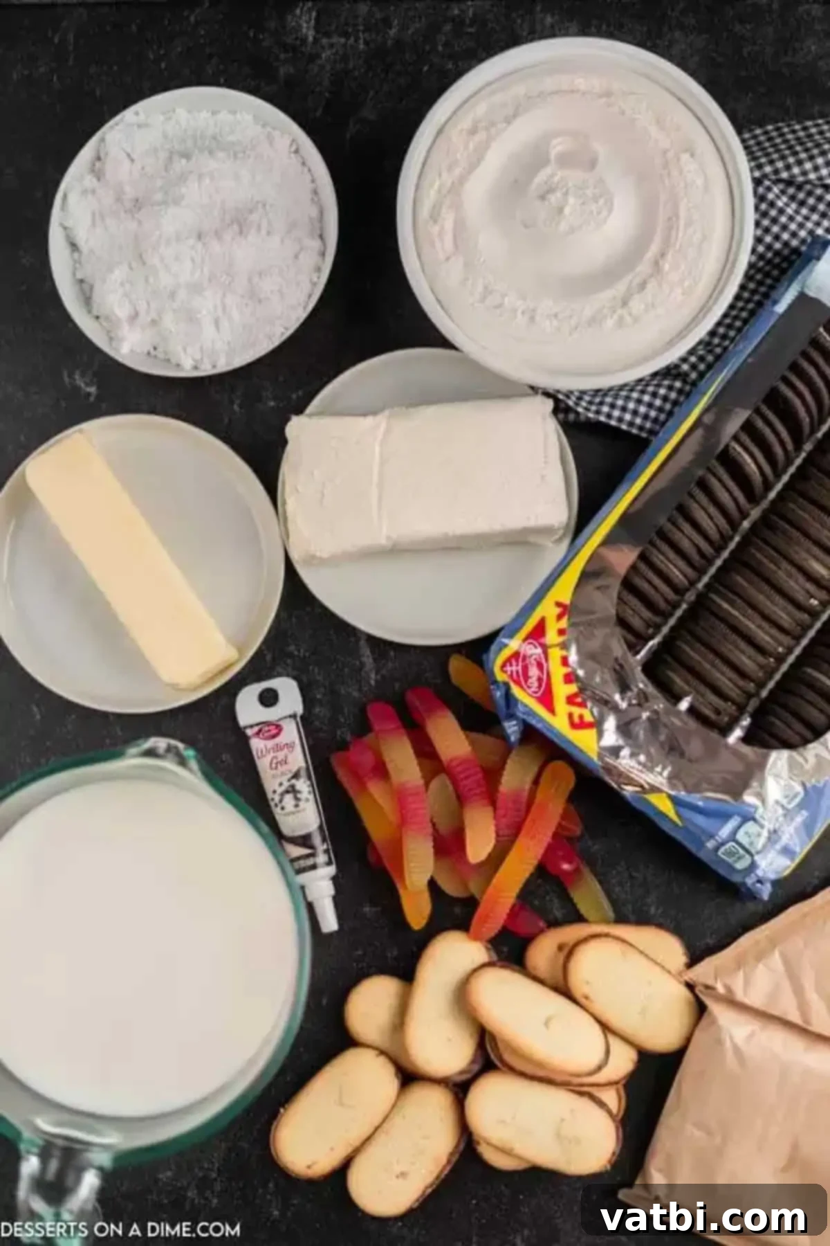 Spooky Halloween Dirt Cake 3 A flat lay of ingredients for Halloween Dirt Cake, including Oreo cookies, cream cheese, butter, powdered sugar, cool whip, instant chocolate pudding mix, milk, Milano cookies, gummy worms, candy pumpkins, and black writing icing.