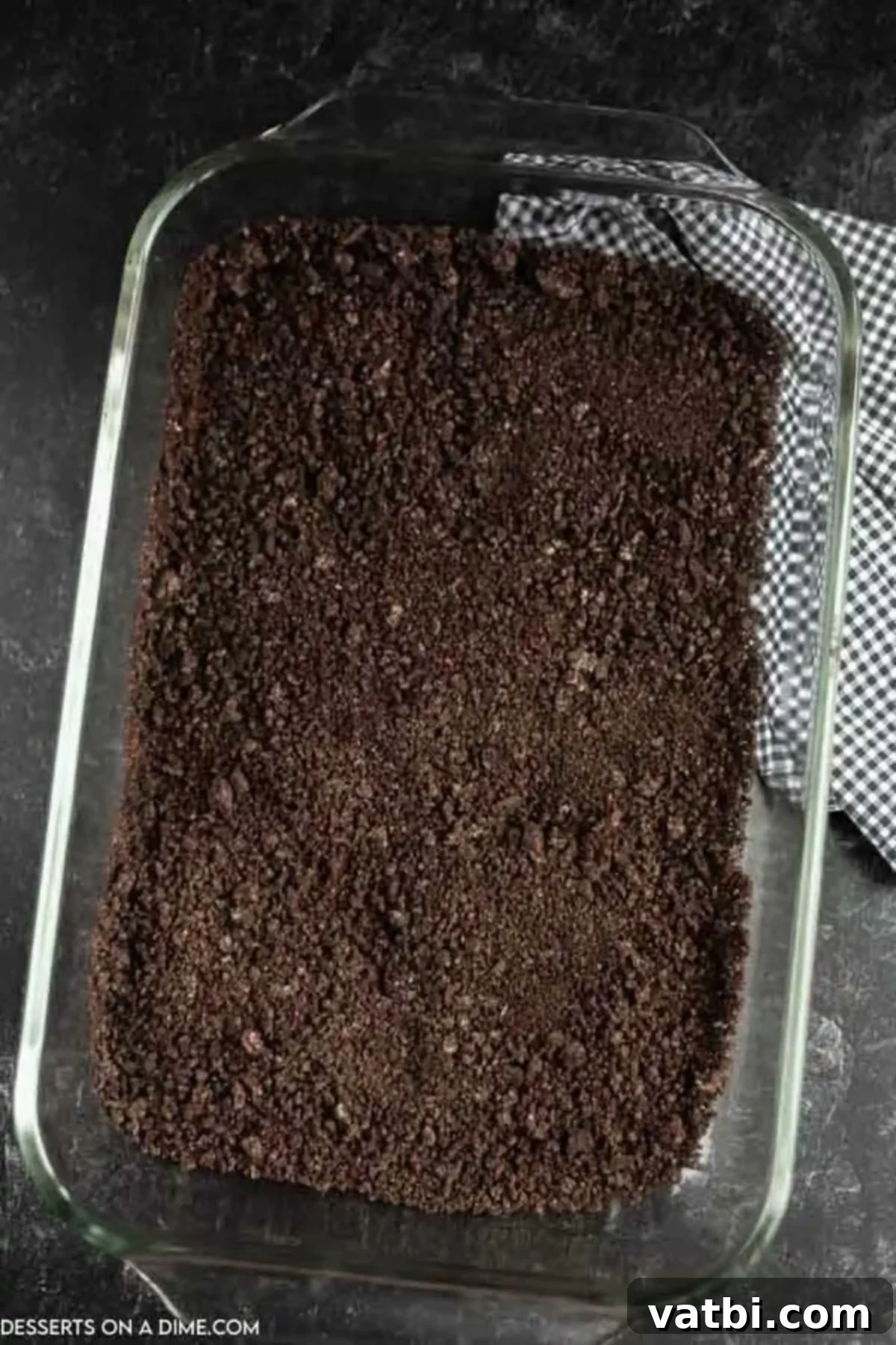 Spooky Halloween Dirt Cake 6 Crushed Oreo cookie crumbs neatly spread across the bottom of a 9x13 baking dish, forming the base layer for the dirt cake.