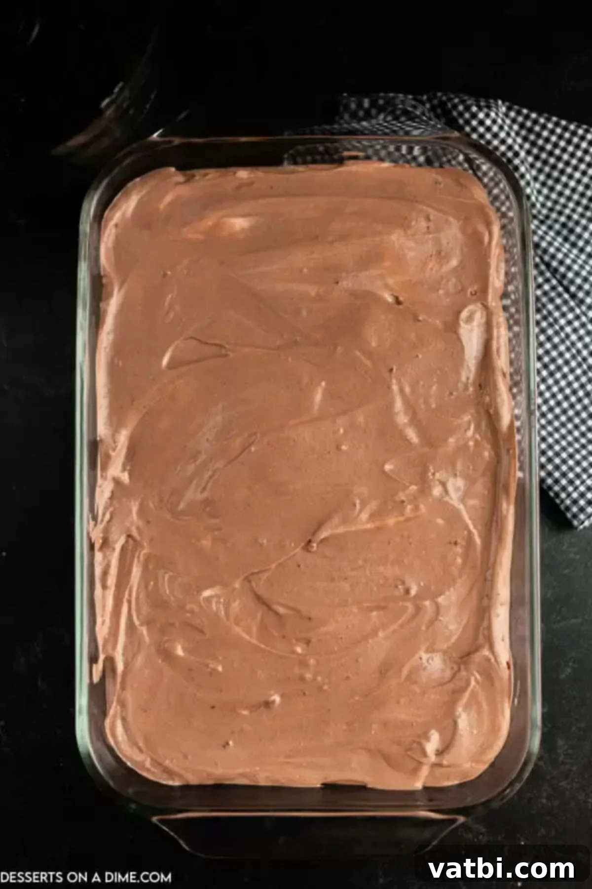 Spooky Halloween Dirt Cake 9 The creamy chocolate pudding mixture being poured and spread evenly over the initial layer of crushed Oreo cookies in a baking dish.